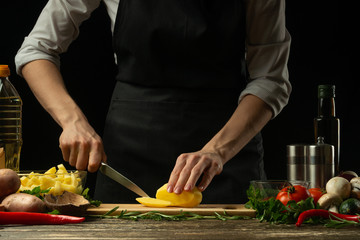 The chef prepares french fries, on the background with vegetables. Preparation of tasty but harmful food