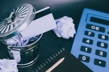 payment card thrown in the trash next to huge calculator and notepad