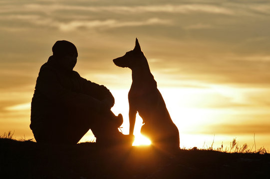 A man and a dog on the background of a beautiful sunset