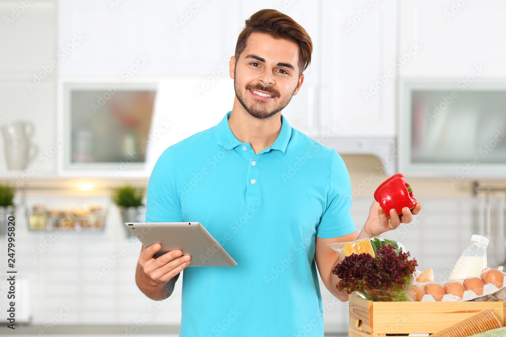 Sticker Young man with tablet PC and products in kitchen. Food delivery service