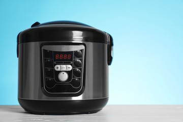 Modern electric multi cooker on table against color background. Space for text