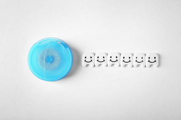 Small plastic teeth with cute faces and dental floss on white background, top view