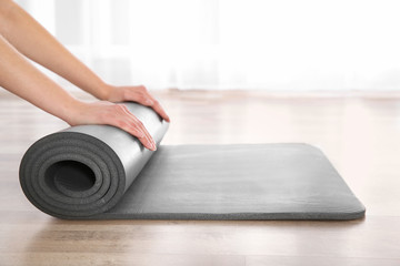Fototapeta premium Woman rolling yoga mat on floor indoors, closeup