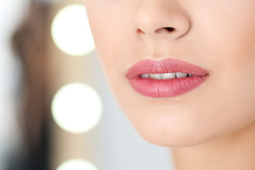 Young woman wearing beautiful lipstick on blurred background, closeup. Space for text