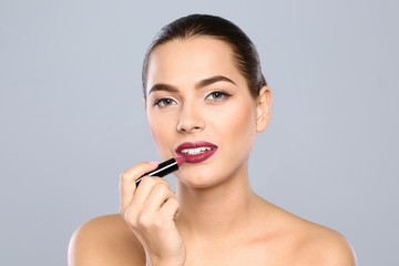 Young woman applying lipstick on color background