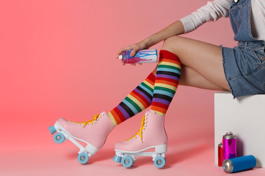 Woman with vintage roller skates and spray paint cans on color background, closeup