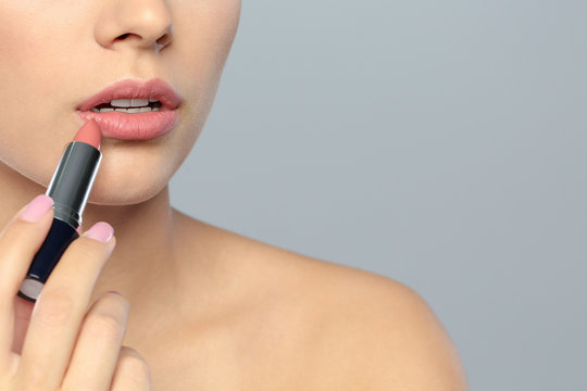 Young woman applying lipstick on color background, closeup. Space for text
