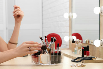 Woman reaching for organizer with cosmetic products and makeup accessories on dressing table indoors, closeup