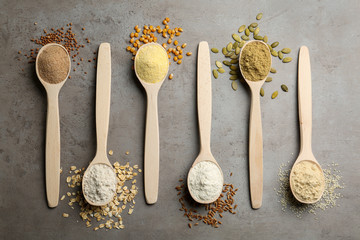 Spoons with different types of flour and ingredients on grey table, top view