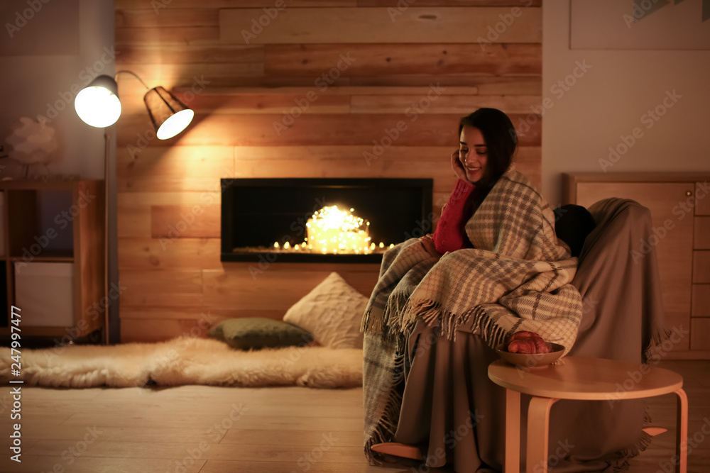 Wall mural Young woman resting near decorative fireplace at home. Winter season