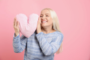 Portrait of mature woman with decorative heart shaped pillow on color background