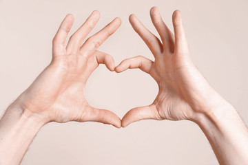 Young man making heart with his hands on light background, closeup
