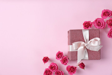 Beautiful roses and gift box on color background, top view. Space for text