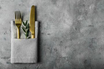 Golden cutlery with napkin on grey background