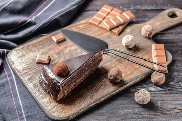 Board with piece of tasty chocolate cake on wooden table