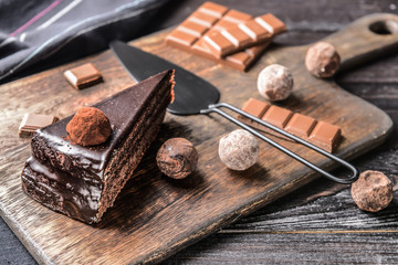 Wooden board with piece of tasty chocolate cake on table