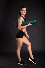 Full length portrait of a young fitness woman in sportswear posing isolated over black background
