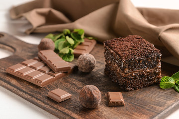 Wooden board with piece of tasty chocolate cake on table
