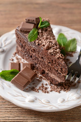 Plate with piece of tasty chocolate cake on wooden table