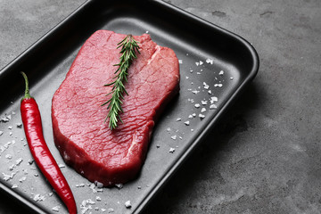 Container with tasty raw meat on grunge background