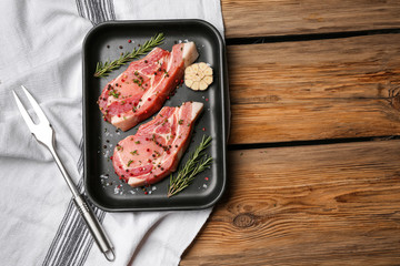 Container with tasty raw meat and spices on wooden background