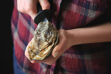 Woman opening raw oyster with knife, closeup