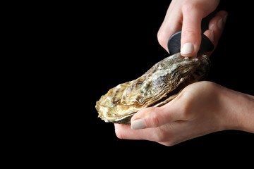 Woman opening raw oyster with knife against dark background