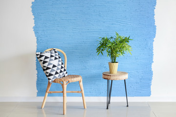 Rattan chair with plant on wooden table near wall in room
