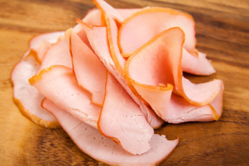Sliced meat pieces, bacon, cold boiled pork, balyk on a white plate. Snack. Meat dish. Closeup. On a wooden board, isolated. On a wooden background.