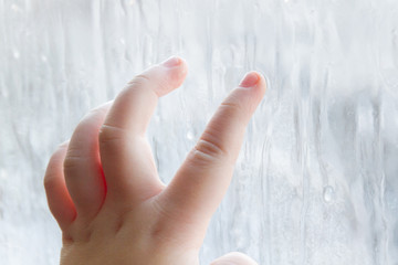 The child's hand draws patterns on the frozen window in winter