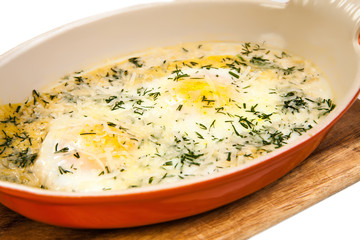 Omelette. Baked scrambled eggs in the oven, sprinkled with herbs and shabby cheese. Delicious breakfast in ceramic form for baking on a wooden board. Isolated on white background