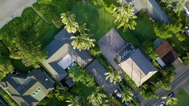 Aerial drone looking down over luxury houses in Hawaii near Lanikai Beach on Oahu. At the beach the camera slowly pans up to reveal two tropical islands.