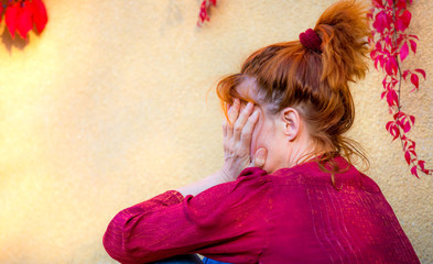 a woman with red hair sits under wild wine and sadly hides her face in her hands