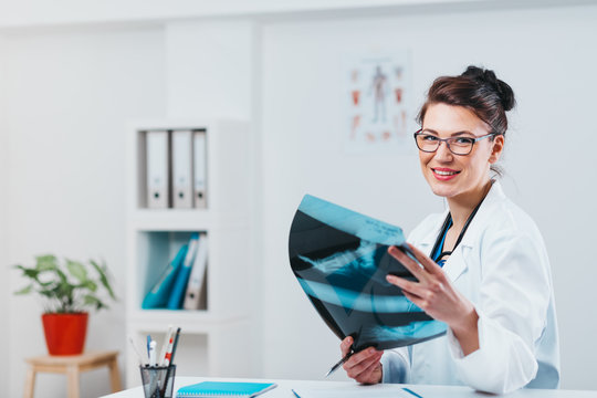 Radiology Specialist looking at x-ray exam. Friendly woman doctor working in her office