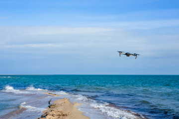 Drone flying in the sky above the waves of the blue sea, which splash on the sandy shore.