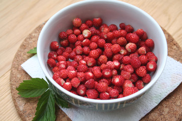 Fresh wild strawberries in a bowl on wooden table