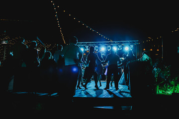 Many people dance outdoors. Colorful lights illuminate.