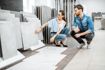Beautiful young couple choosing big granite tiles for their house repairment in the building shop