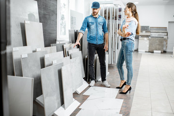 Young woman customer choosing tiles standing with seller or repairman in the ceramic shop