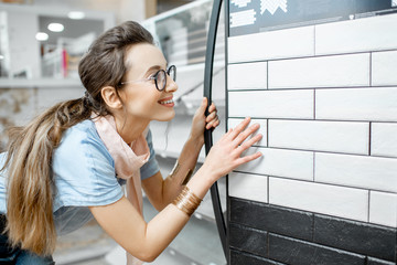 Young woman designer choosing ceramic tiles looking on the exposition in the shop