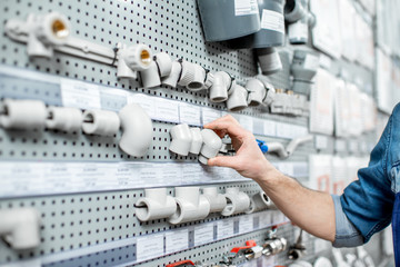 Workman choosing water pipes and pipe joints standing near the showcase in the plumbing shop,...