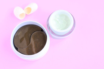 Green face cream and container with black golden anti aging collagen lifting patches under eyes for woman face care and pure silky fiber cocoons with selective focus on pink neutral background 