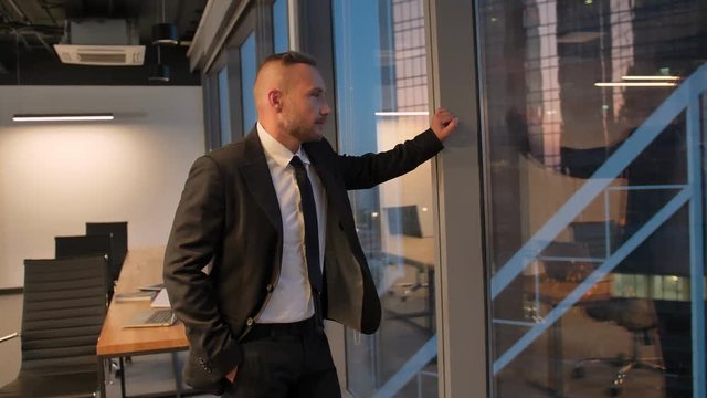 Successful businessman in suit standing in office with hands in pockets, CEO.