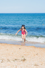 a little girl in a red swimsuit and a black cap dancing on the sandy beach