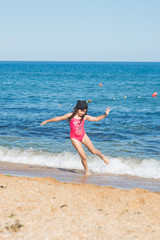 a little girl in a red swimsuit and a black cap dancing on the sandy beach