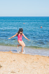 a little girl in a red swimsuit and a black cap dancing on the sandy beach