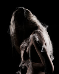 Beautiful topless blonde girl with hair falling on her face, stands sideways covered with spider web, with a her hand covers her big boobs. Black background. Artistic noir silhouette photo