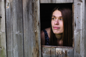 Young woman looks out of the wooden shed windows.