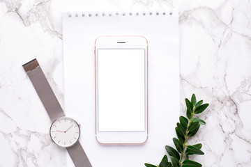 Mobile phone , clock and white notebook on a marble background with greens