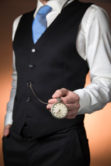 man in elegant suit on orange background holding a pocket watch hanging from his waistcoat